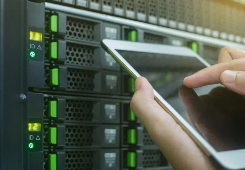 A person holding a tablet in front of some servers.