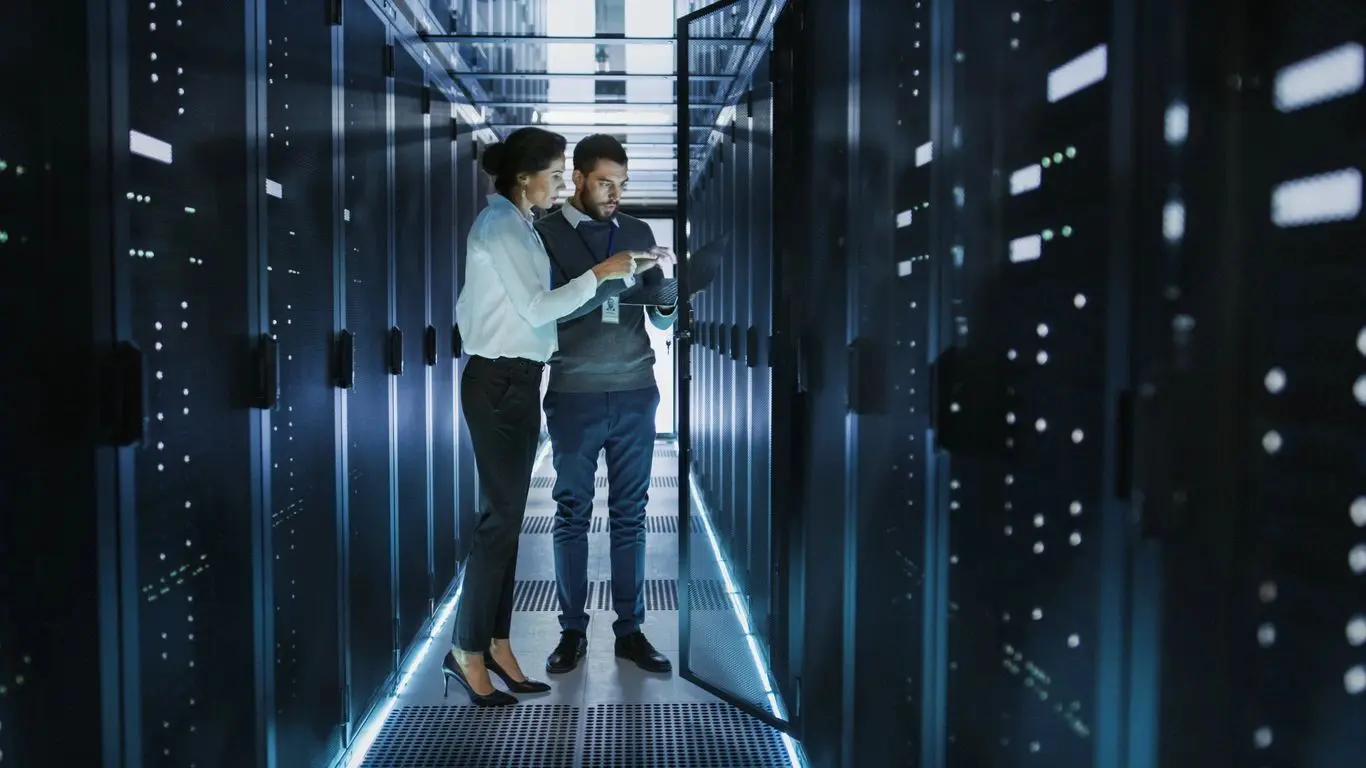 Two people in a room with some racks of servers